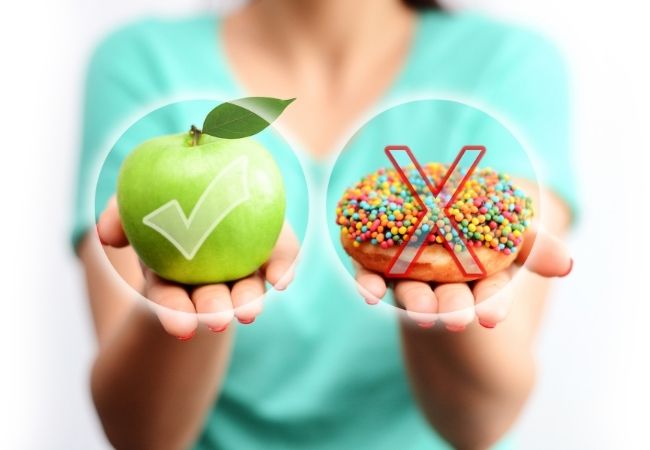 Woman holding both an apple and a donut. An x is placed over the donut and a checkmark is placed of the apple.