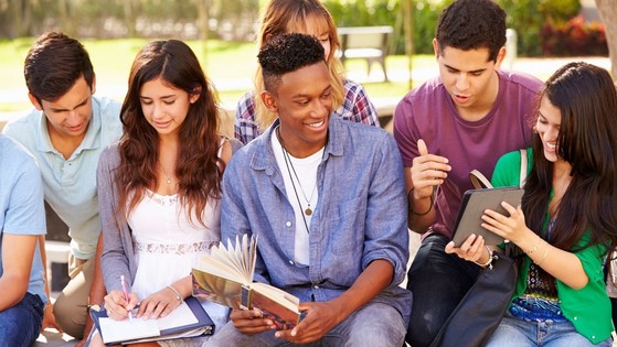 Diverse group of teenagers holding books and tablets in the park