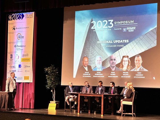 Presenters sitting at a table on a stage at the Symposium