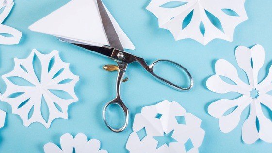 Scissors on a table with snowflakes made from paper