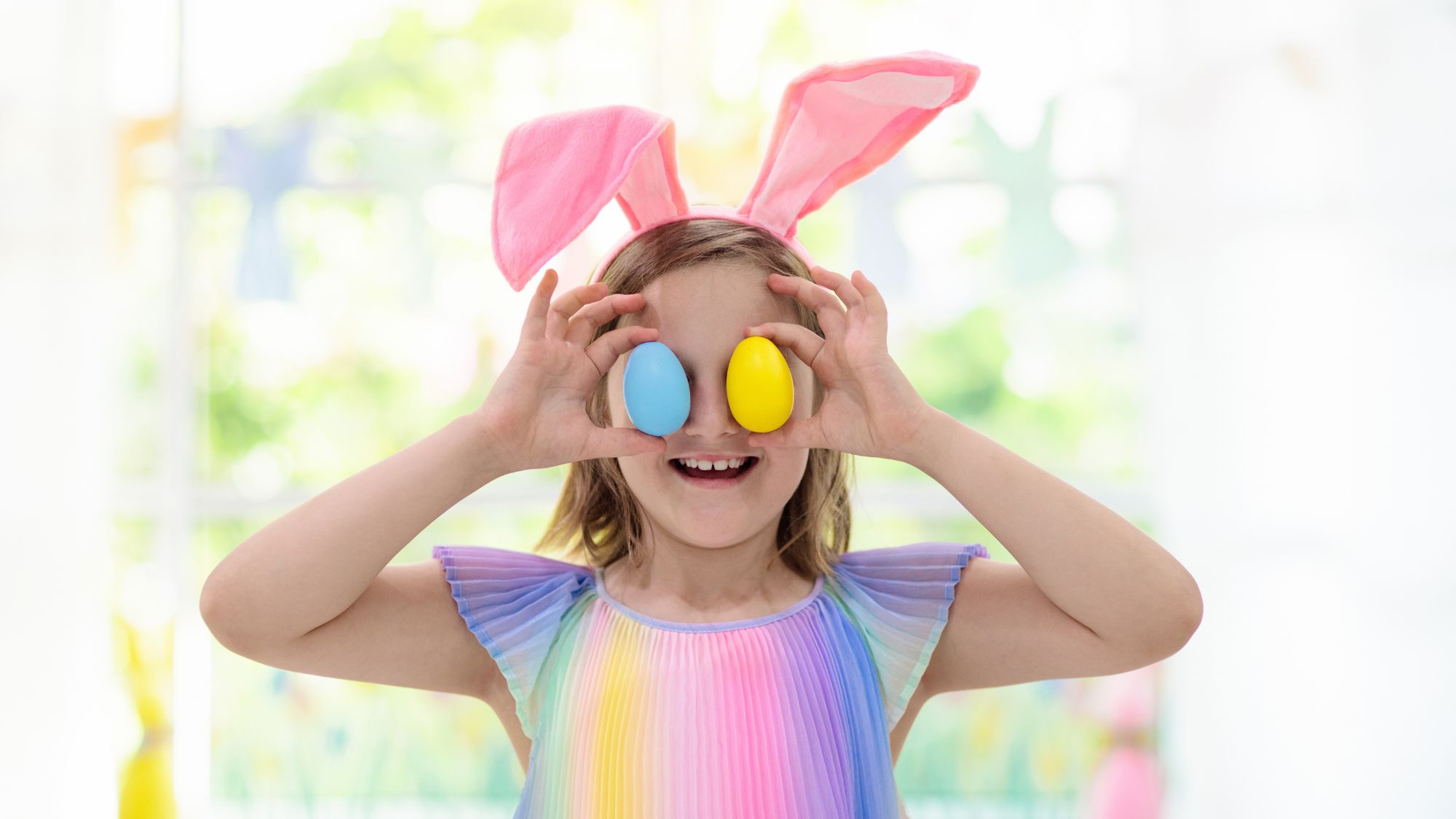 Girl with bunny ears and Easter eggs held on her eyes.