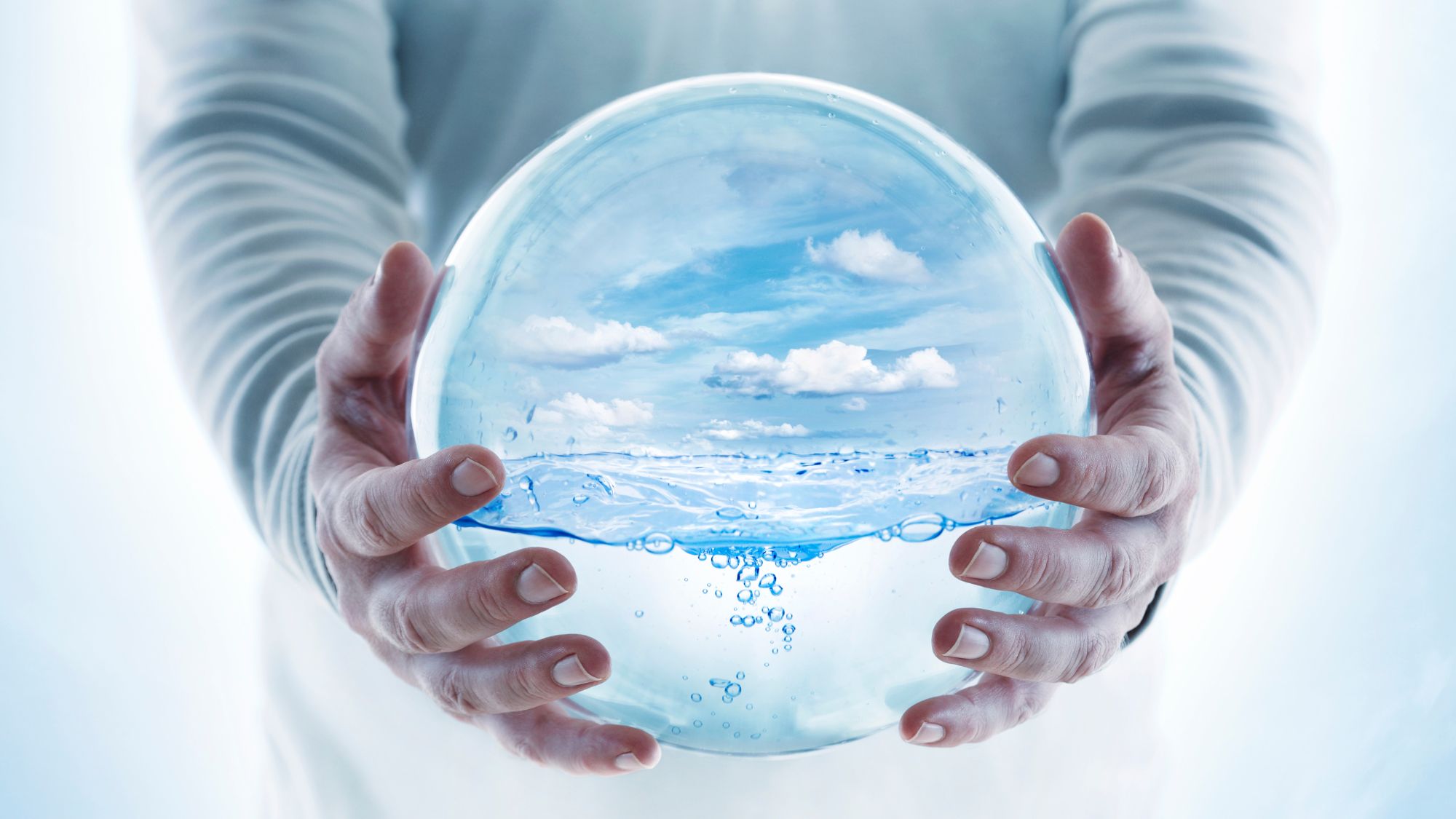 Person holding clear globe with water and sky inside